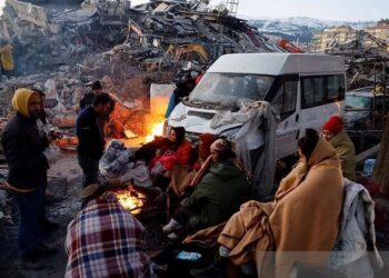 Orang-orang duduk di sekitar api di samping puing-puing dan kerusakan di dekat lokasi bangunan yang runtuh setelah gempa bumi, di Kahramanmaras, Turki, (08/02/2023). (Foto: Ant/Reuters/Suhaib Salem/pri).