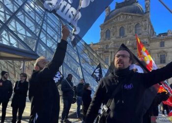 Para pengunjuk rasa memegang bendera serikat pekerja CGT dan Sud Culture Solidaires Prancis berdiri di depan Piramida kaca untuk memblokir pintu masuk Museum Louvre untuk memprotes reformasi pensiun pemerintah Prancis, di Paris, Prancis, Senin (27/03/2023). (Foto: Ant./Reuters-Marco Trujillo/hp).​​​​​​​